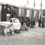 Three wheeler Lambro 200 in front of tent with people in a row